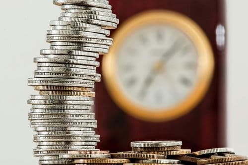 Stack of coins in front of a blurred clock symbolizing time and money management, representing budgeting, saving, and cash flow planning.